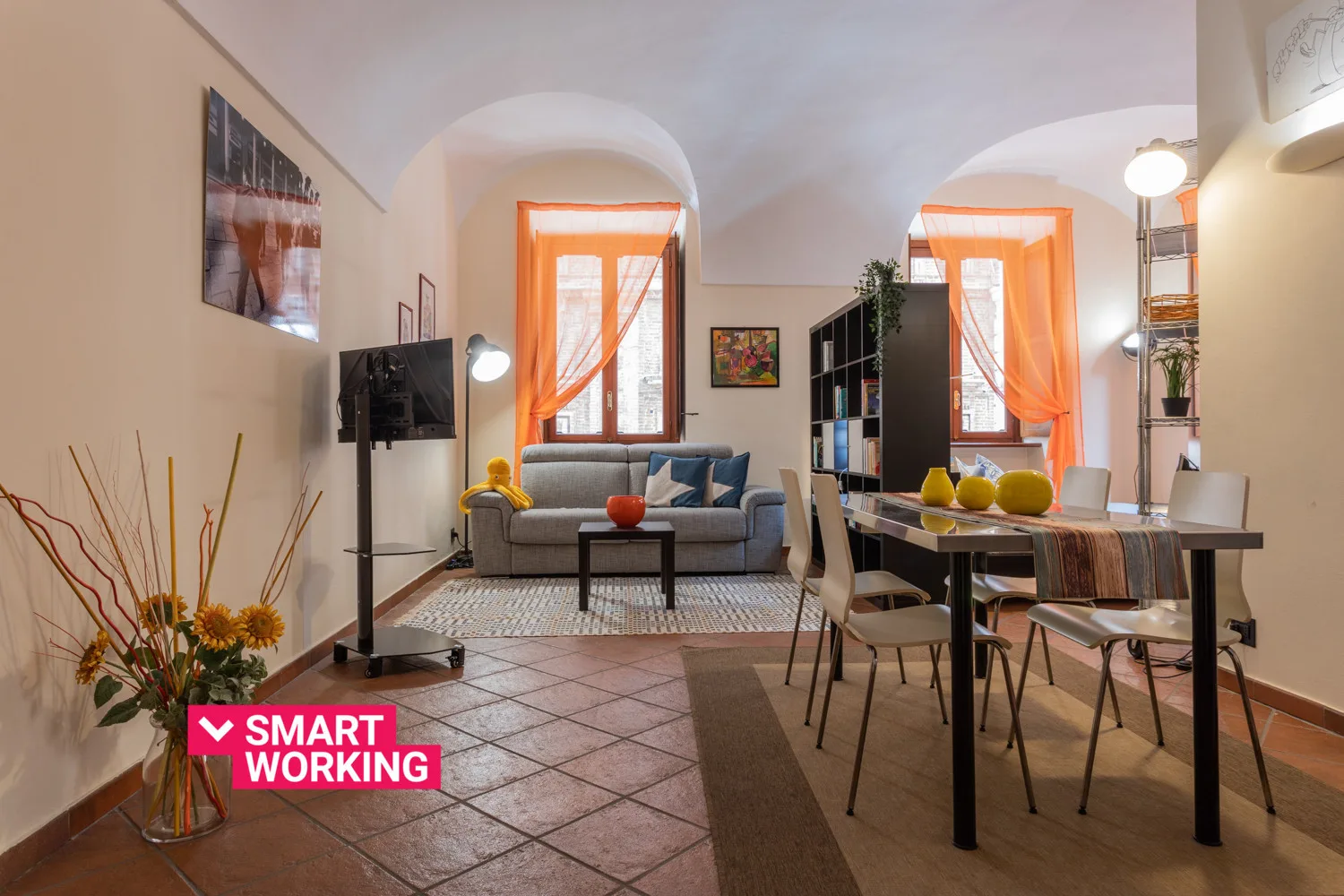 Una sala de estar y comedor con sofá, mesa y ventanas luminosas con cortinas.