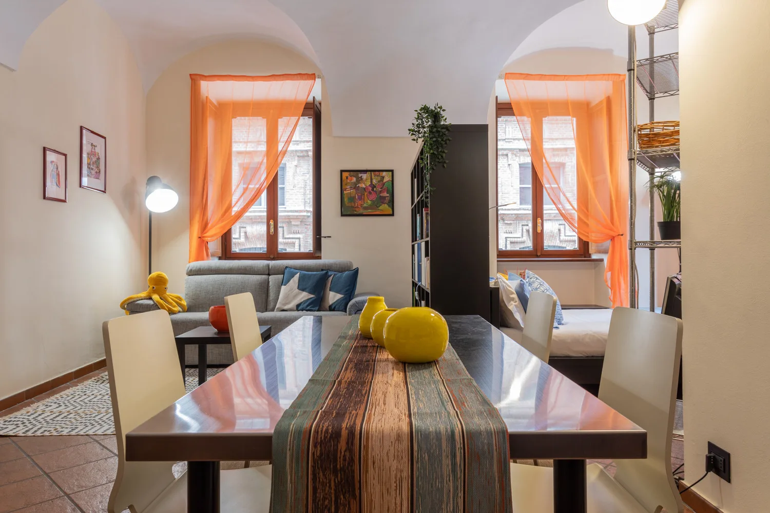 Un comedor con una mesa larga, asientos y cortinas naranjas luminosas.