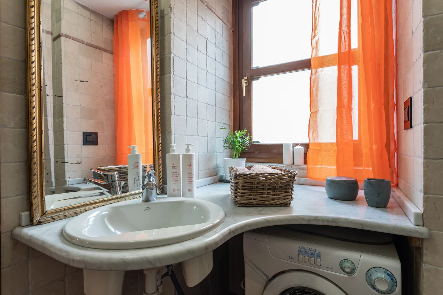 A bathroom vanity with a sink sits beneath a window with orange curtains.