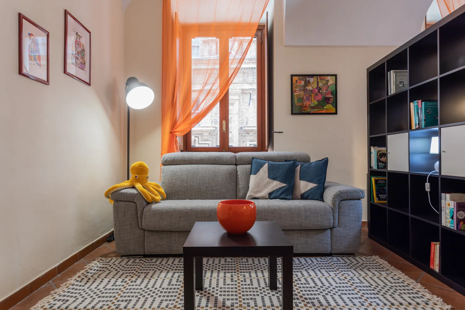 Una sala de estar con asientos grises, una mesa de centro y cortinas naranjas.