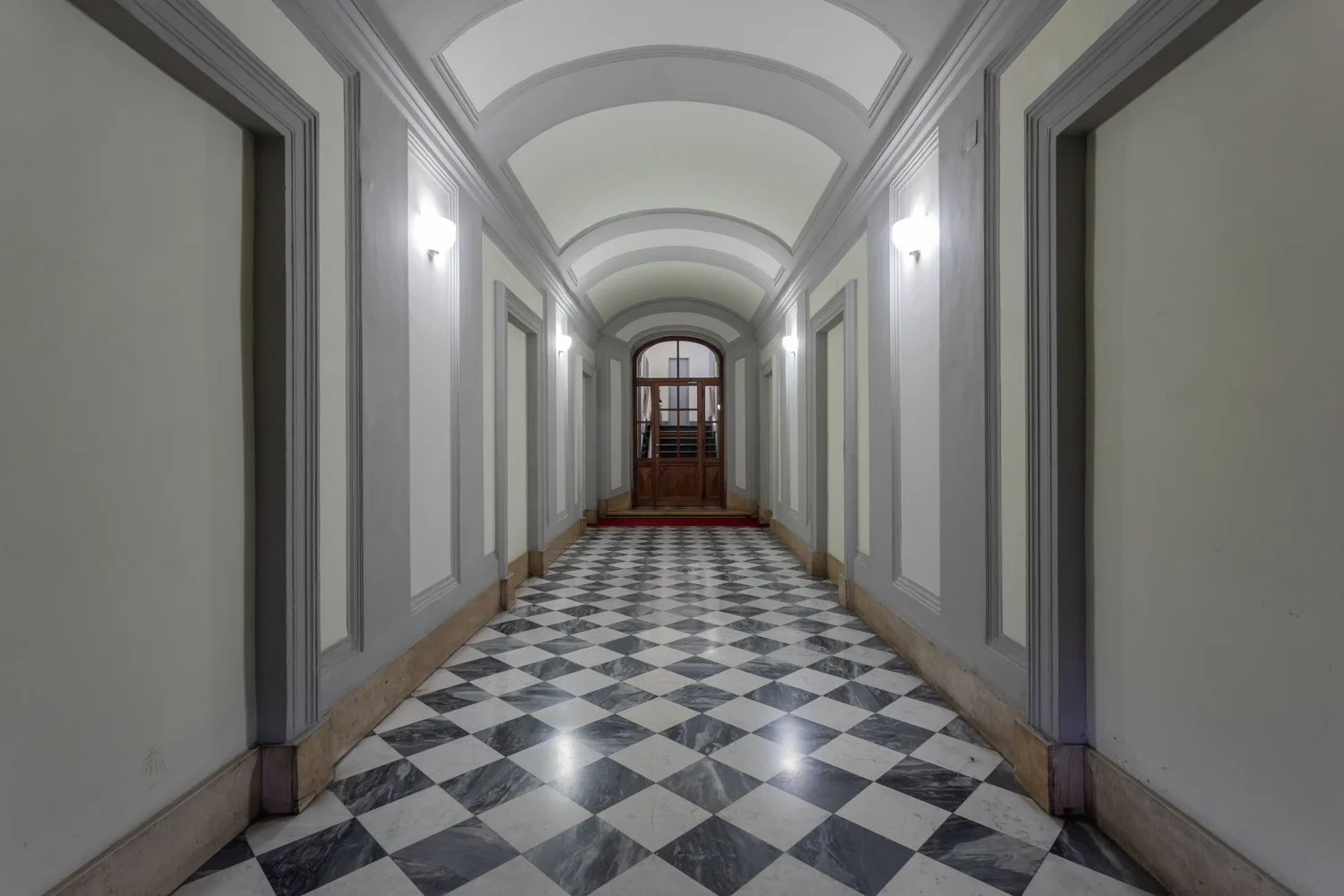Un largo pasillo interior con suelo a cuadros blancos y negros y techo abovedado.