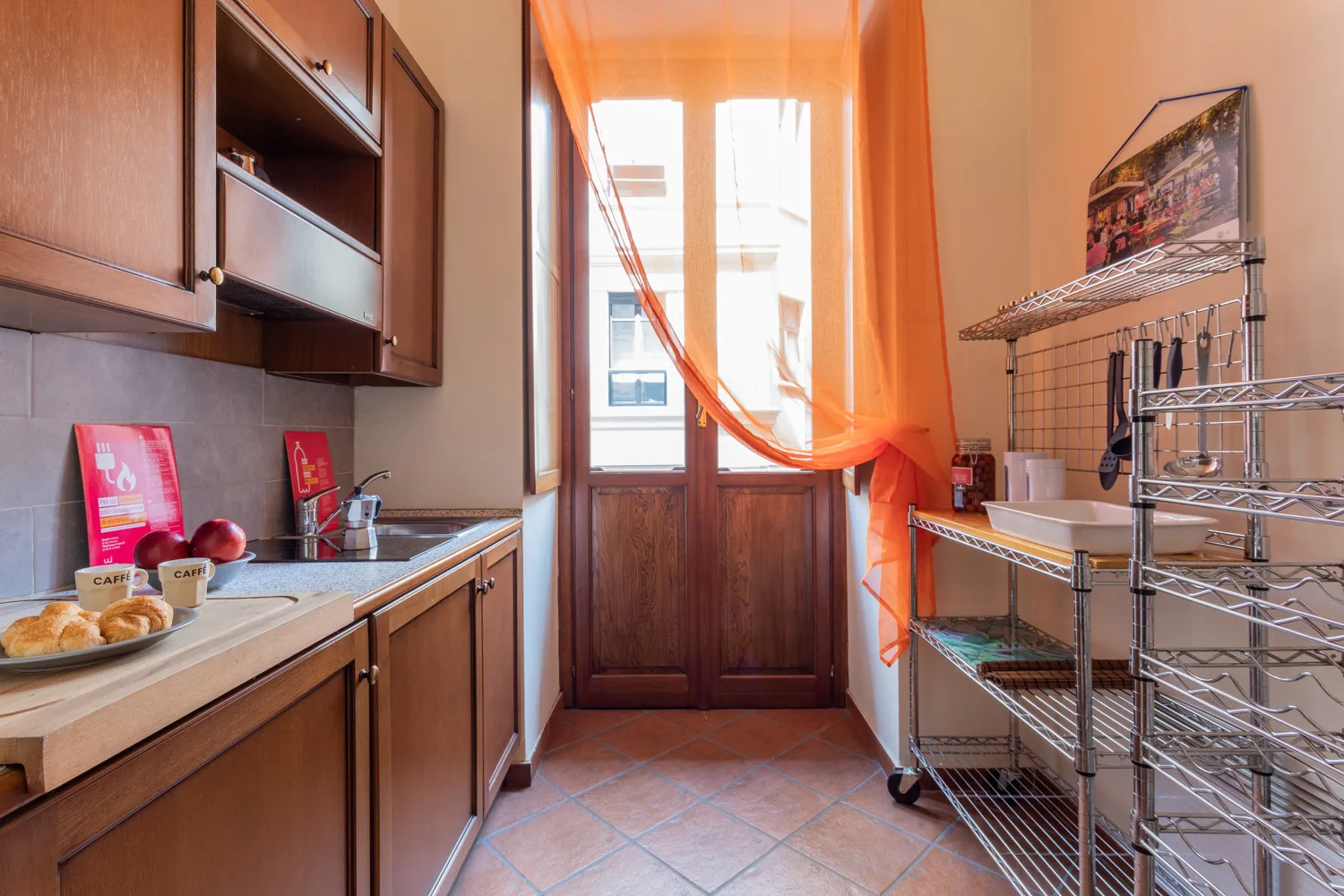 A kitchen with wooden cabinets, a countertop, and a curtained window.