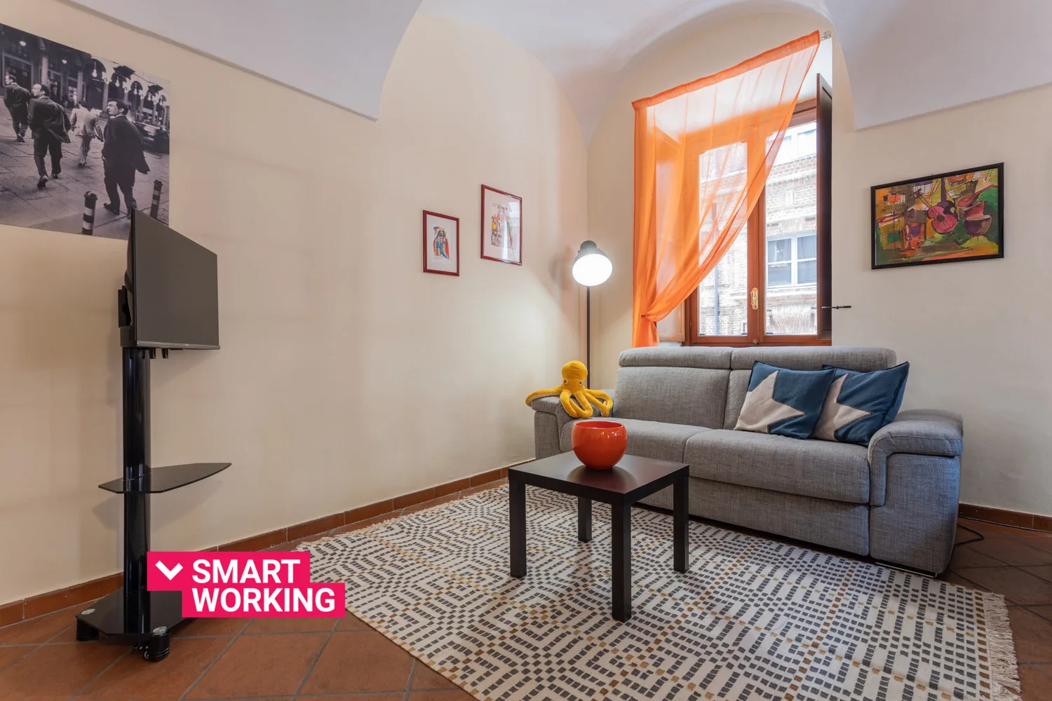 Una sala de estar con un sofá gris, una alfombra estampada y cortinas naranjas.