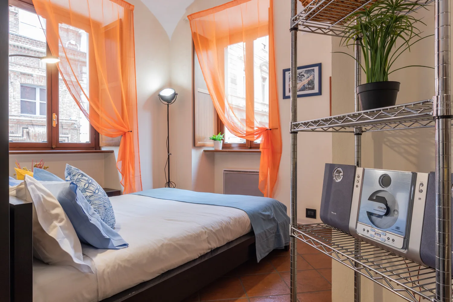 A bedroom with a bed beneath bright windows and orange curtains.