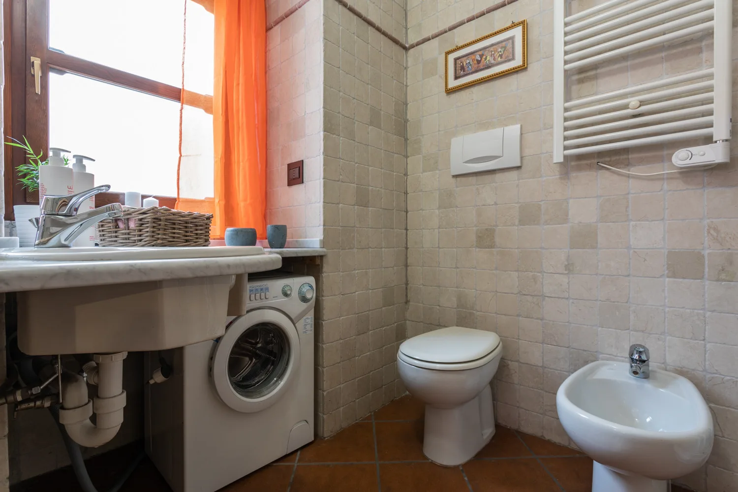 Un baño con azulejos, inodoro, bidé y lavadora debajo del lavabo.