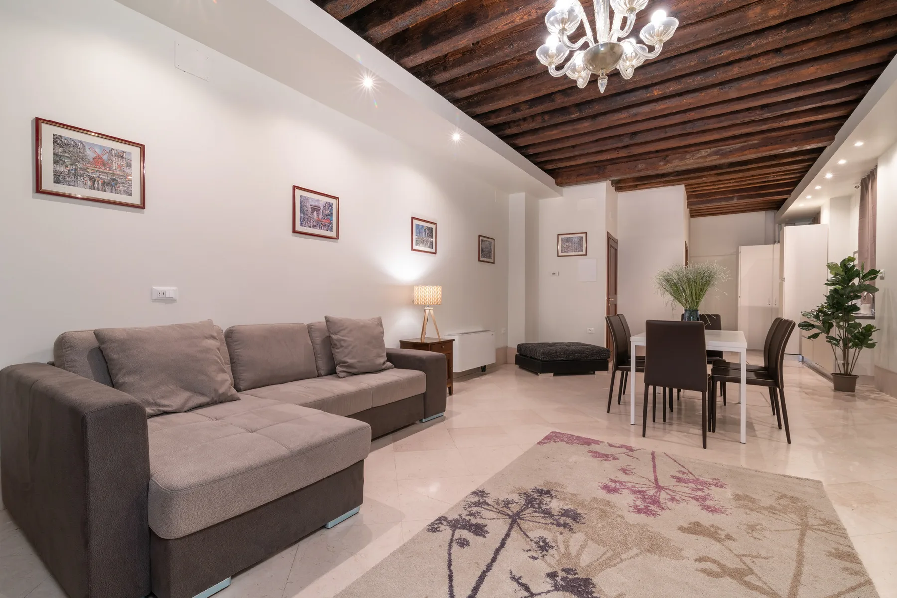 Sala de estar y comedor con asientos grises, una mesa y vigas oscuras a la vista.