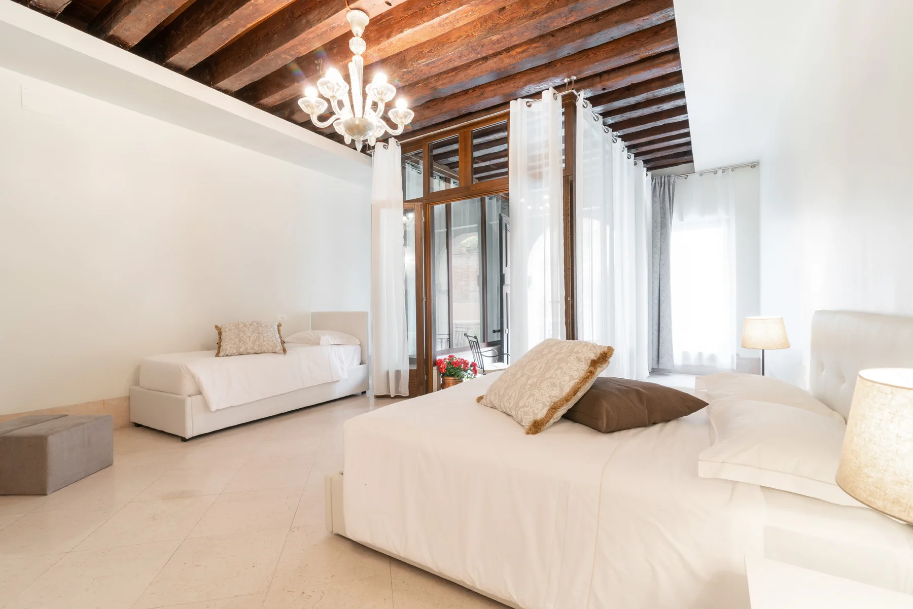 Un dormitorio luminoso con una cama grande, un sofá y ventanas altas con cortinas.