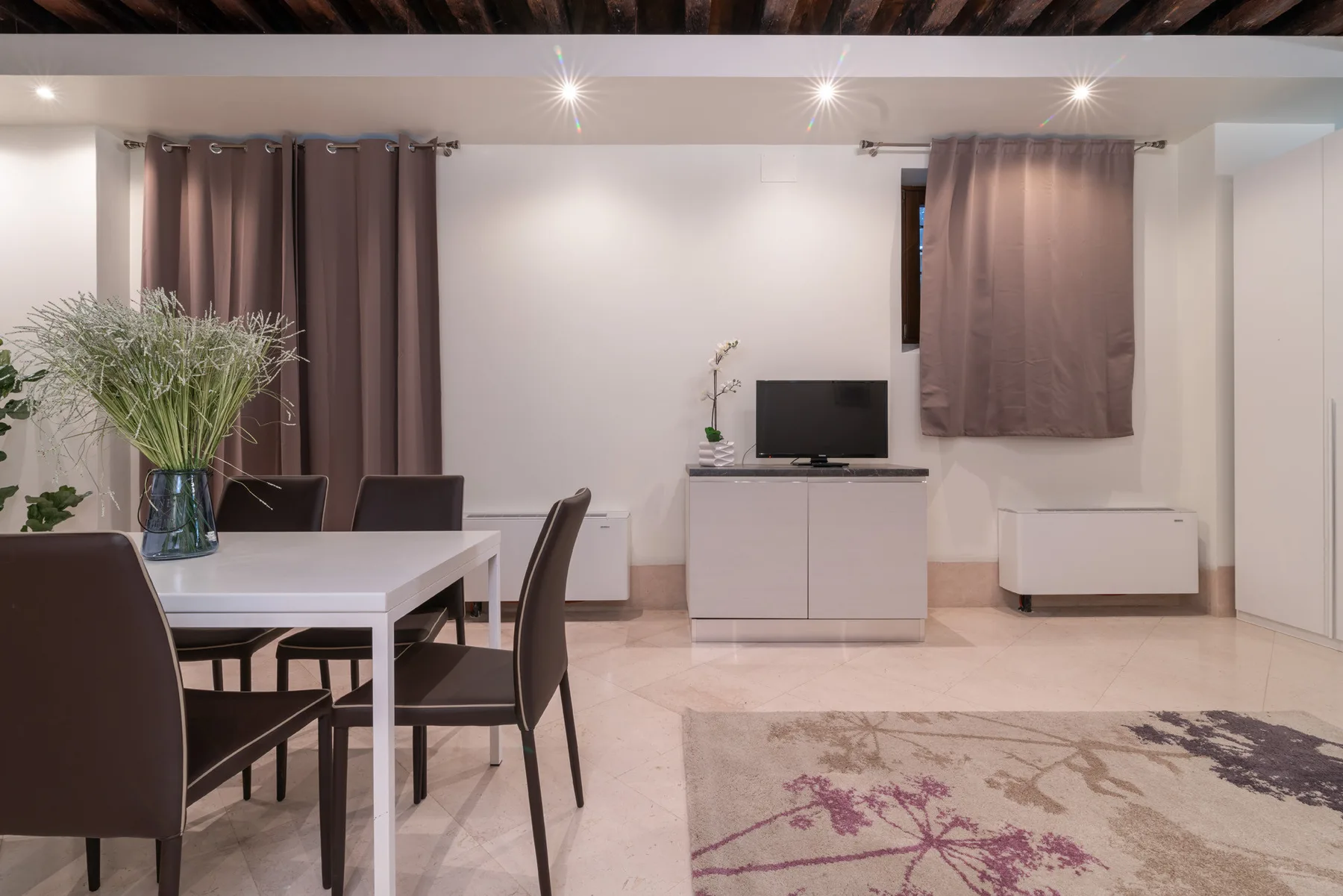 Una zona de comedor y estar con una mesa, un televisor y una alfombra.