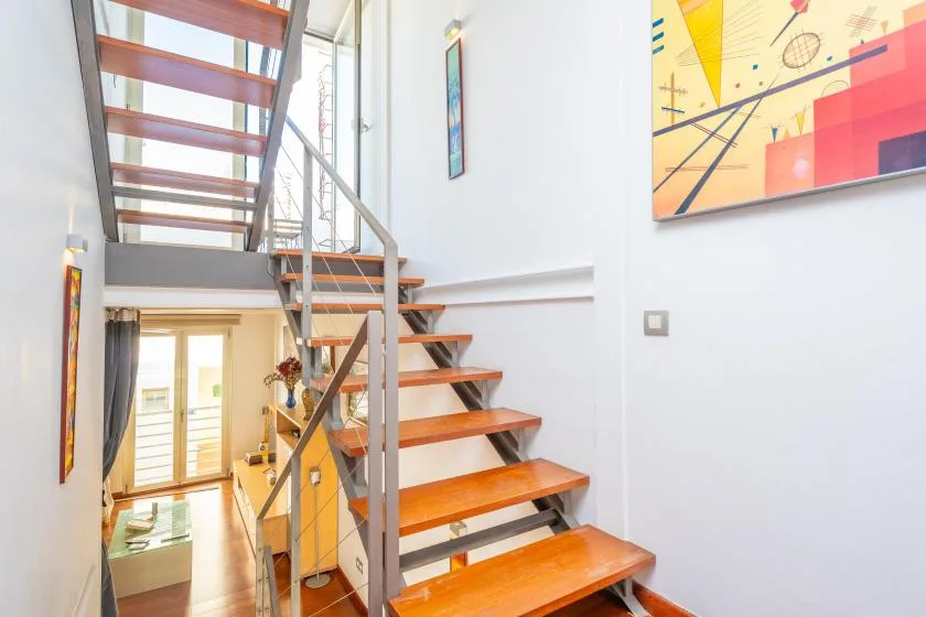 A bright interior stairway with wooden steps, metal railings, and framed artwork.
