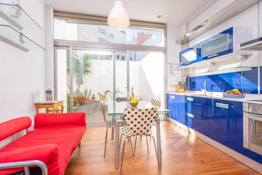 A bright open-plan living and kitchen area with red seating and blue cabinets.