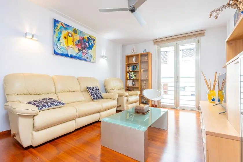 A bright living room with beige seating, a glass coffee table, and balcony doors.