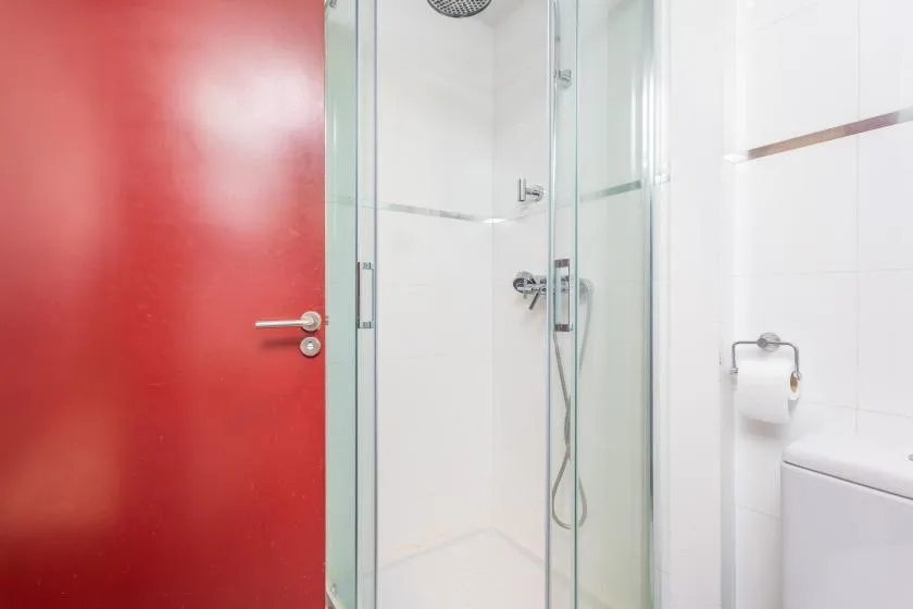 A tiled bathroom with a glass shower and a red door.