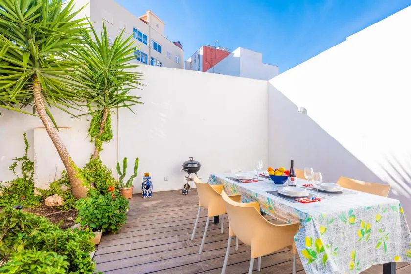 An outdoor dining area with a set table beside leafy plants and white walls.