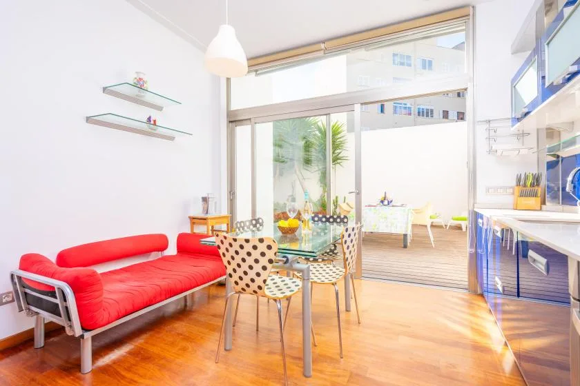 A bright dining and kitchen area with a table, red seating, and large windows.