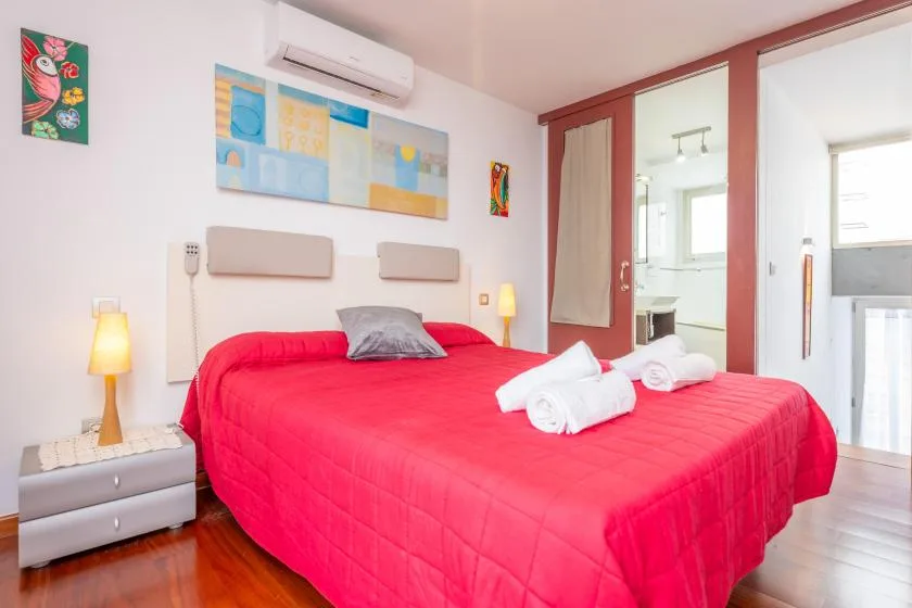 A bedroom with a bright red bedspread and colorful wall art.