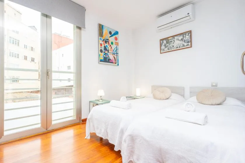 A bright bedroom with two beds beside large glass doors.