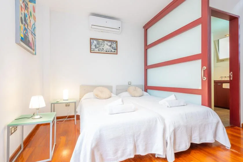 A bright bedroom with two beds beside a red-framed partition.
