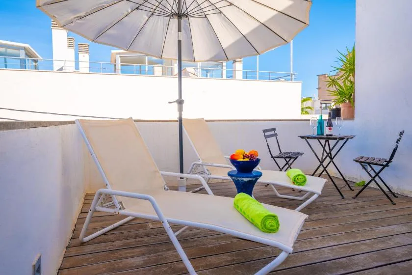 A sunny rooftop terrace with lounge seating, a large umbrella, and a small table.
