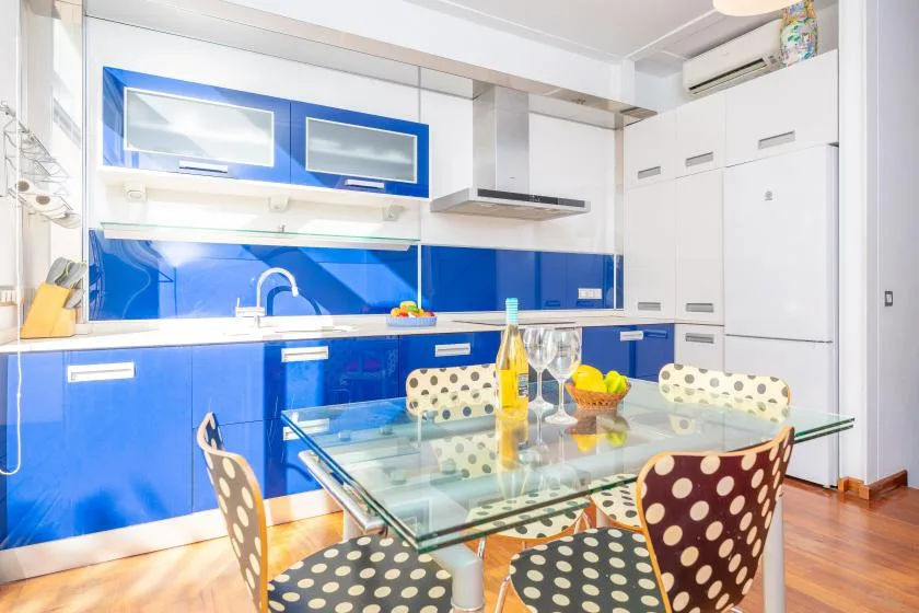 A bright kitchen and dining area with blue cabinets and a glass dining table.