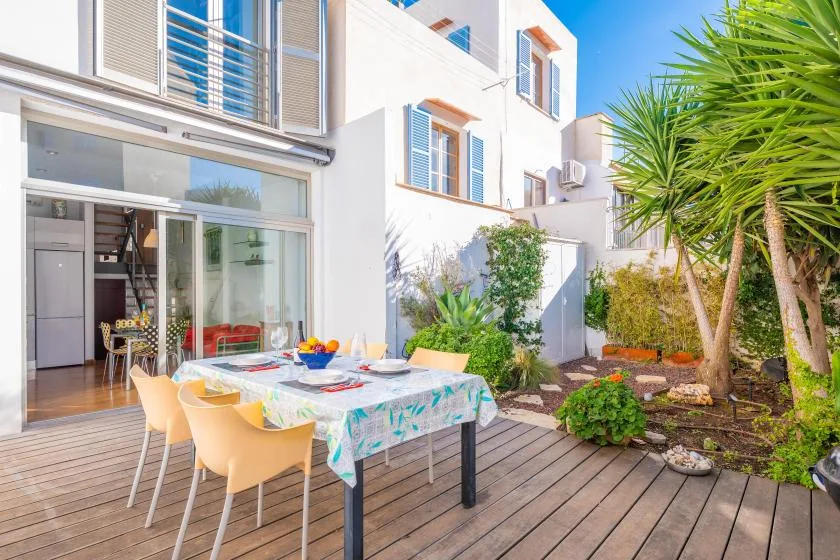An outdoor dining table sits on a wooden deck beside a bright building.