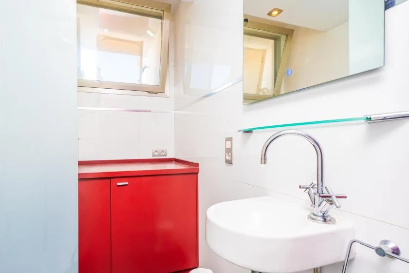 A bathroom vanity with a white sink, red cabinet, and wall mirror.
