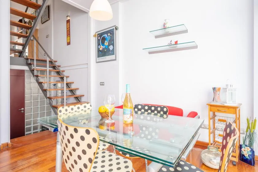 A dining area with a glass table and a staircase along the wall.