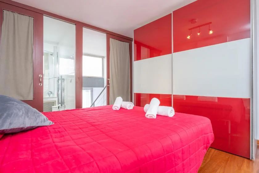 A bedroom with a bright red bedspread and mirrored wall panels.