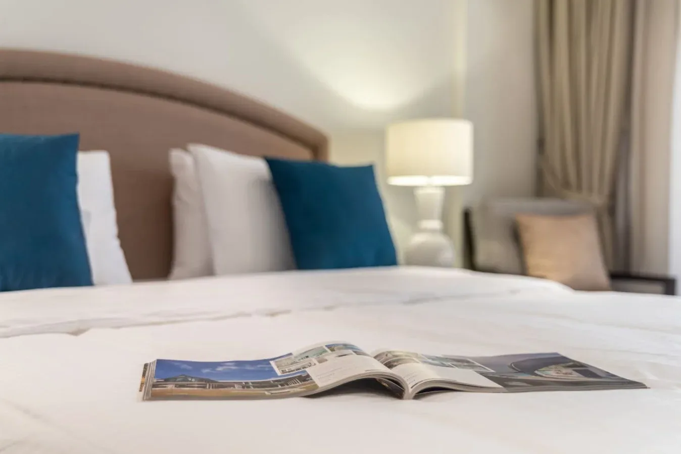 Un dormitorio con una cama bien tendida, cojines azules y una lámpara de noche.