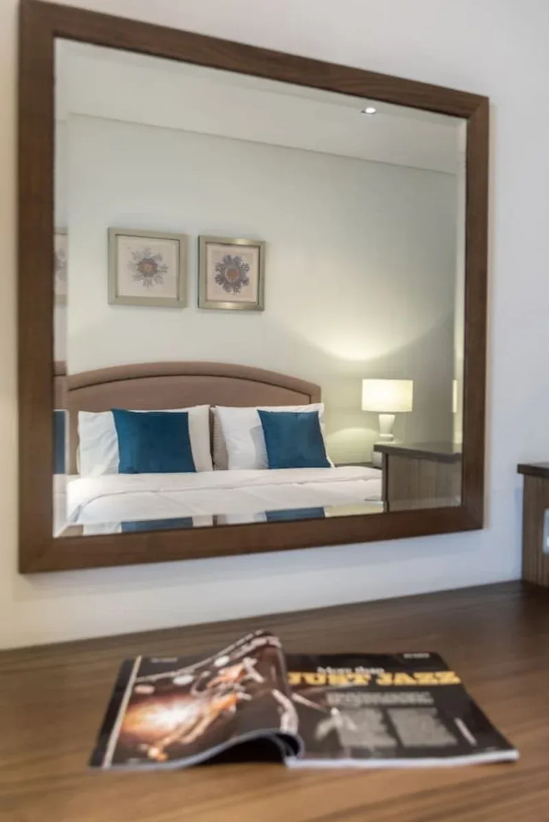 Un dormitorio reflejado en un espejo grande, con una cama y cuadros enmarcados.
