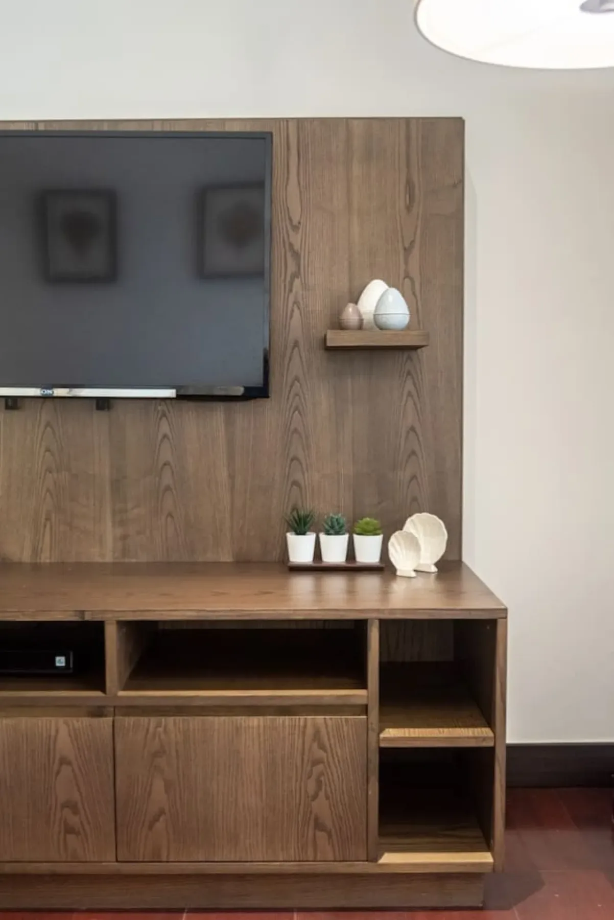 Un televisor montado en la pared cuelga sobre un mueble de madera con pequeños objetos decorativos.