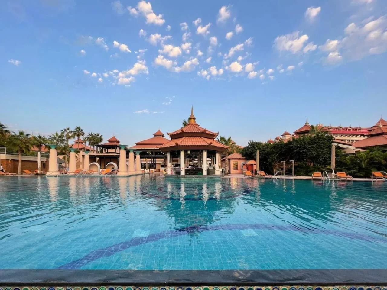 Una piscina se extiende hacia un pabellón de techo rojo bajo un cielo azul.