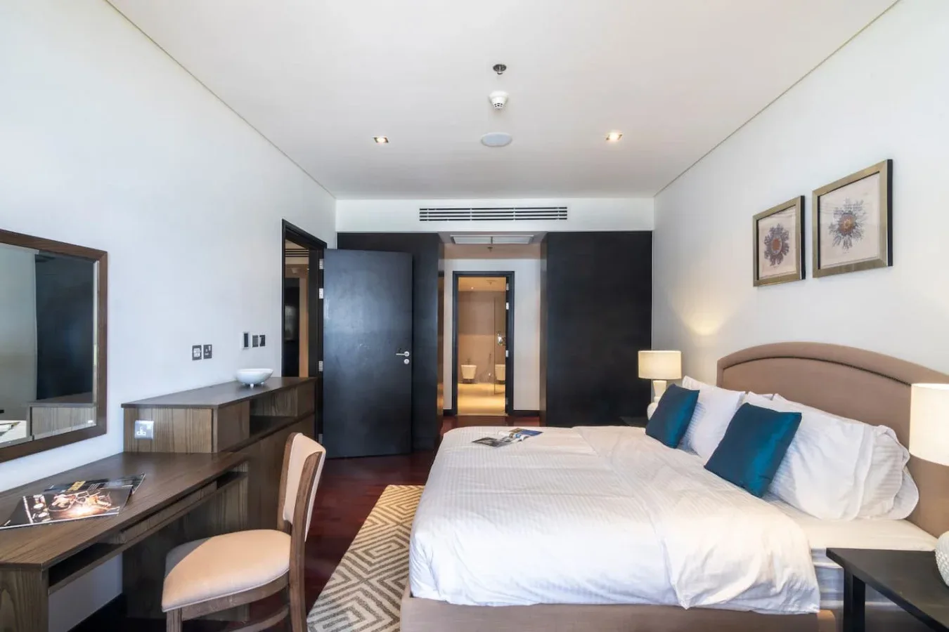 Un dormitorio con una cama bien tendida, un escritorio y cuadros en la pared.