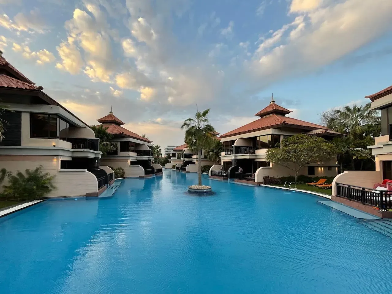 Una gran piscina está rodeada de edificios de estilo turístico bajo un cielo nublado.