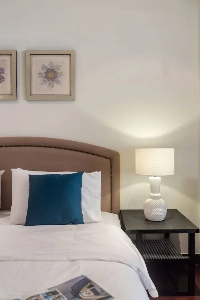Un dormitorio con una cama, un cojín azul y una lámpara de noche.