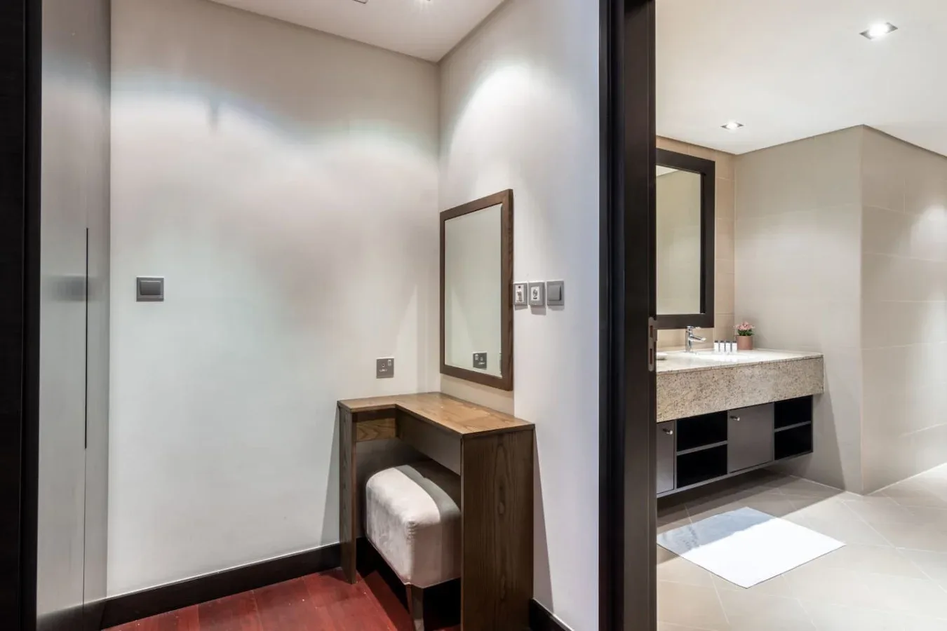 Una zona de tocador de baño con espejo, encimera y asiento acolchado.