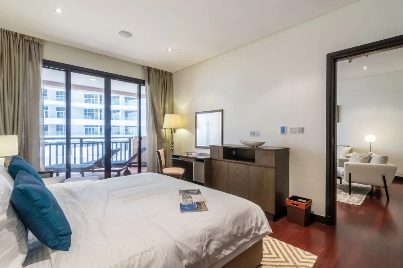 Un dormitorio con una cama grande, asientos junto a la cama y puertas de vidrio hacia un balcón.