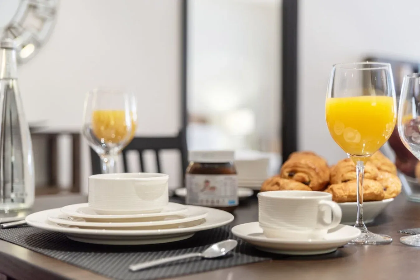 Una mesa de desayuno puesta con tazas, pasteles y vasos de jugo de naranja.