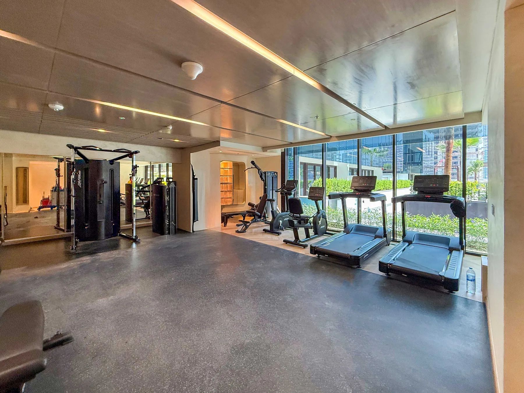 A gym with exercise machines and treadmills beside large windows.