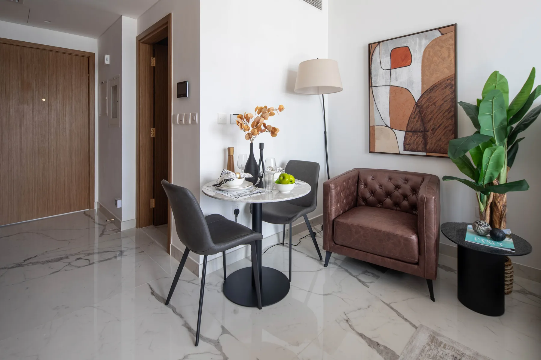 Un comedor con una mesa redonda y sillas junto a un sillón marrón y una planta en maceta.