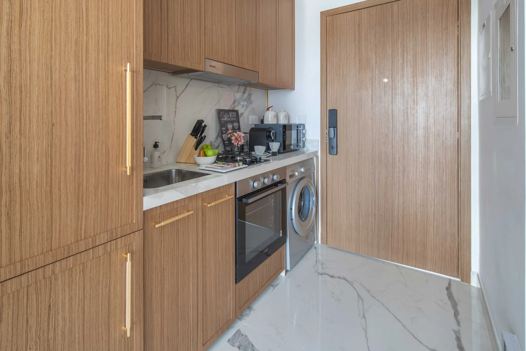 A compact kitchen with wood cabinetry, a countertop, and a washing machine.