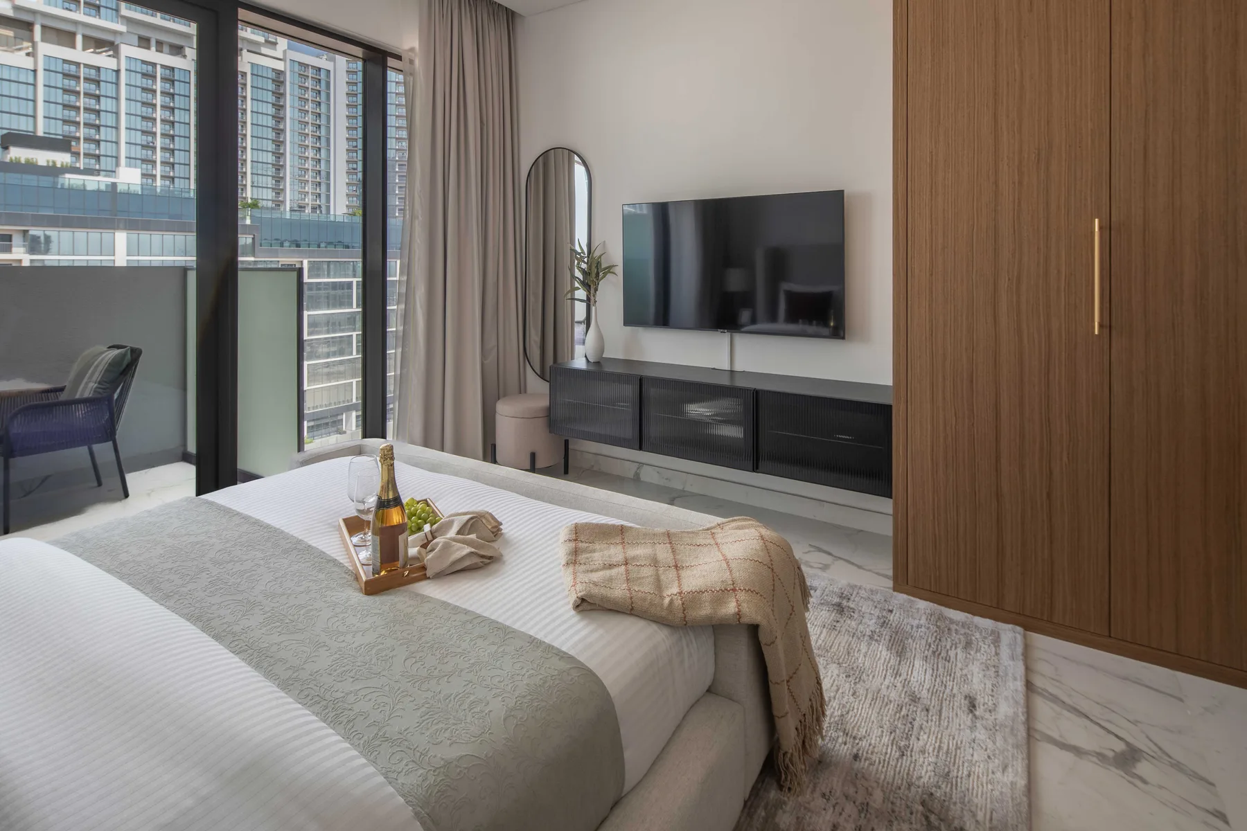 A bedroom with a bed, television, and large windows overlooking nearby buildings.