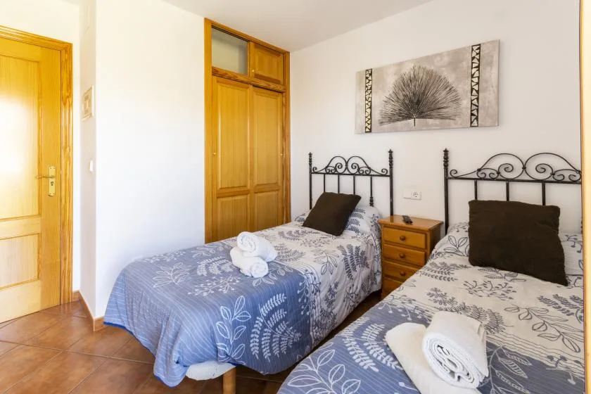 A bedroom with two single beds, patterned bedding, and a wooden wardrobe.