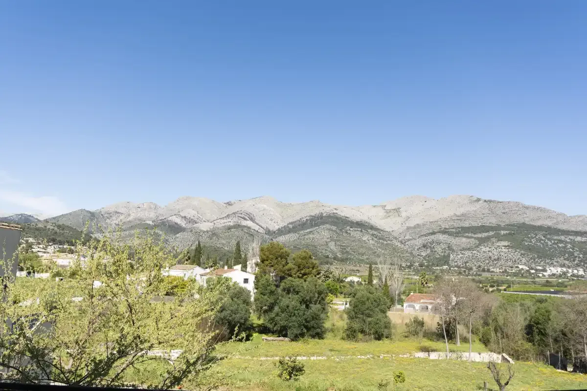 A rural landscape with scattered homes, green fields, and mountains beneath a clear sky.