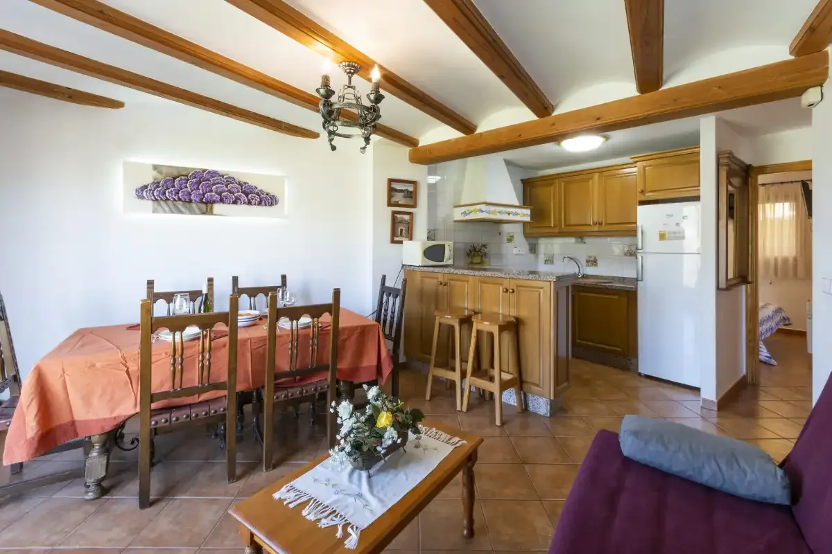 A dining area and compact kitchen share a room with exposed ceiling beams.
