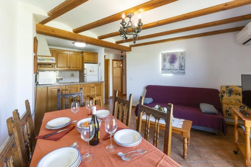 A dining area opens onto a living room with a purple sofa and wooden ceiling beams.