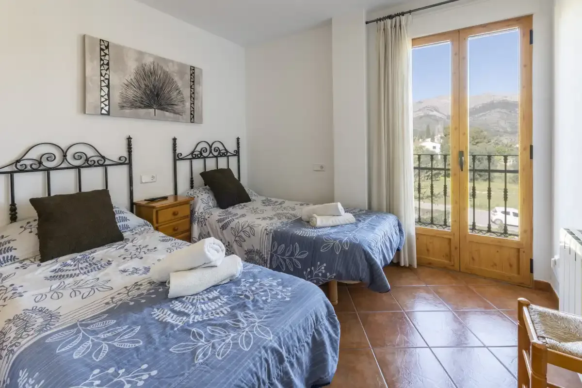 A bedroom with two beds and glass doors opening onto a balcony.