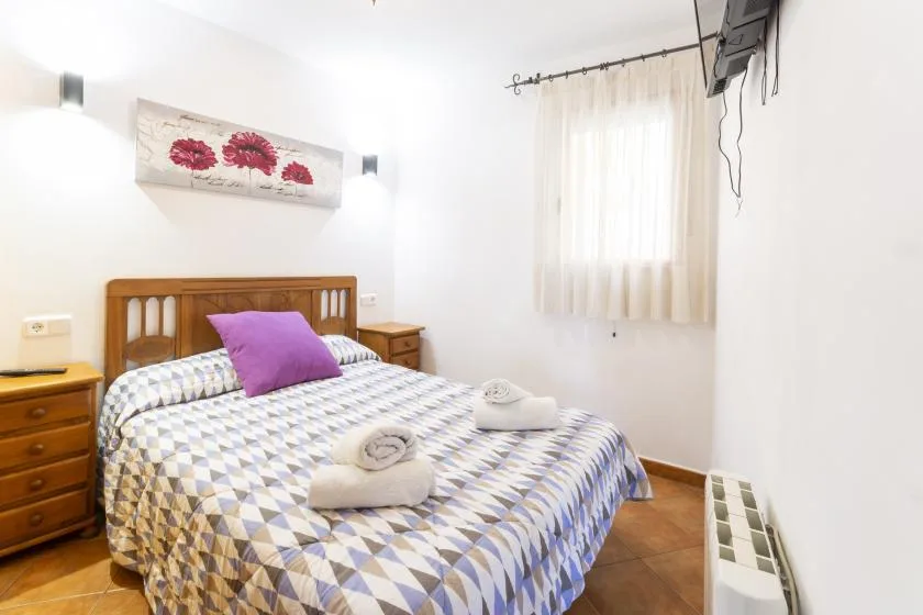 A bedroom with a patterned bedspread and a window with sheer curtains.