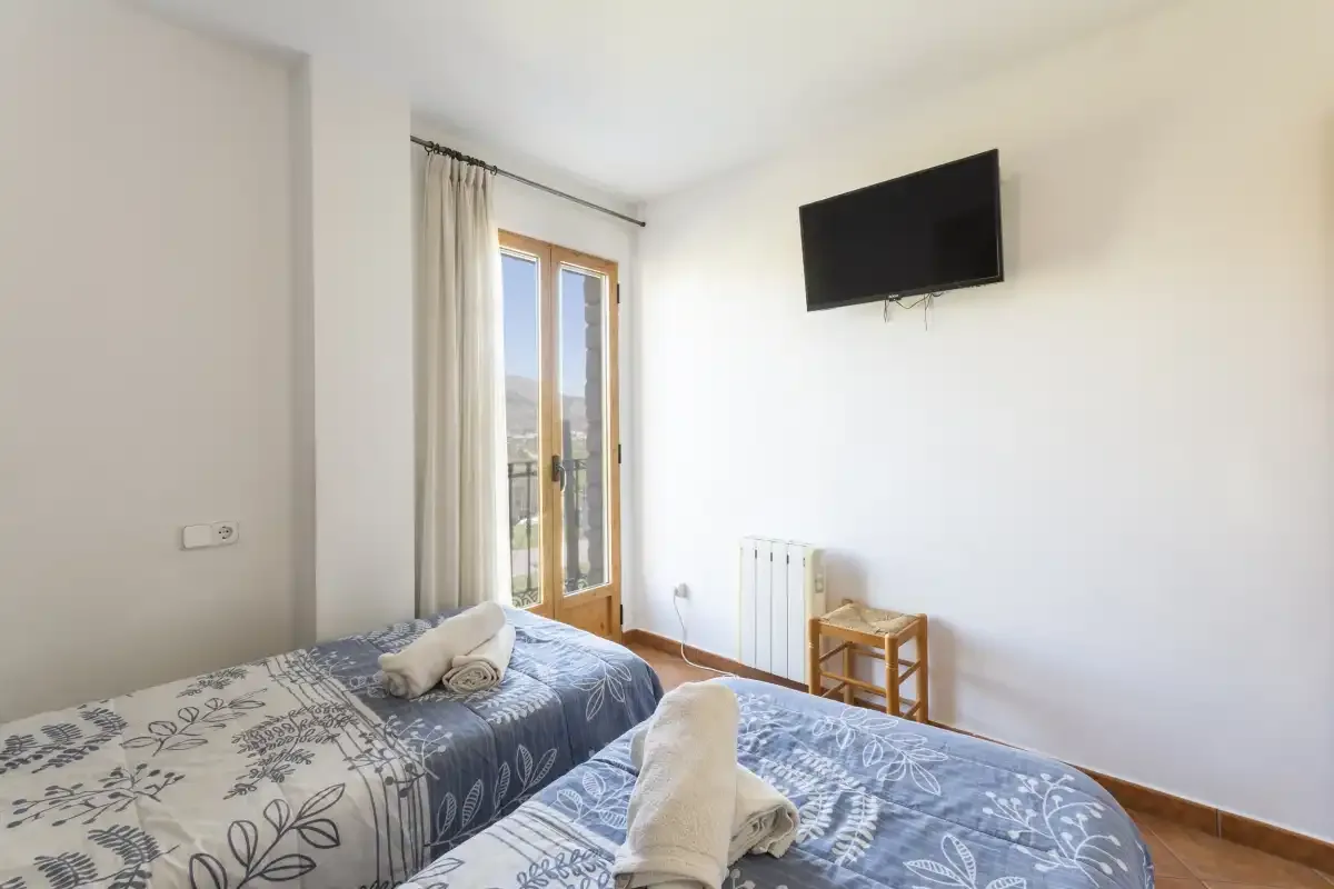 A bedroom with two beds, a wall-mounted television, and glass balcony doors.