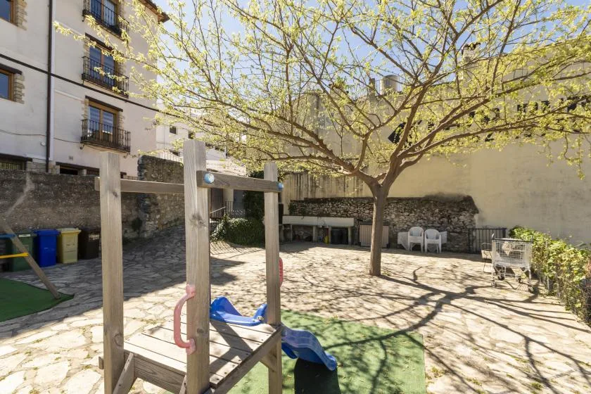 A sunny outdoor courtyard with a leafy tree and a small play area.