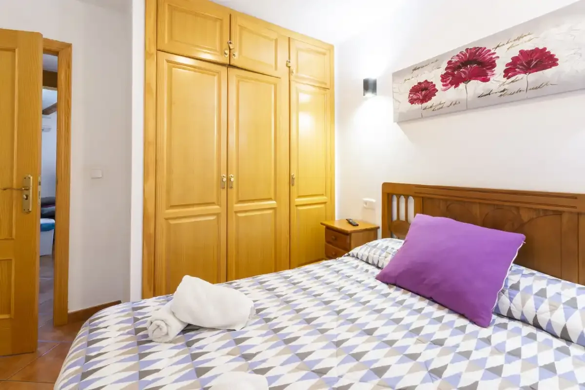 A bedroom with a wooden bed, patterned bedding, and a purple pillow.
